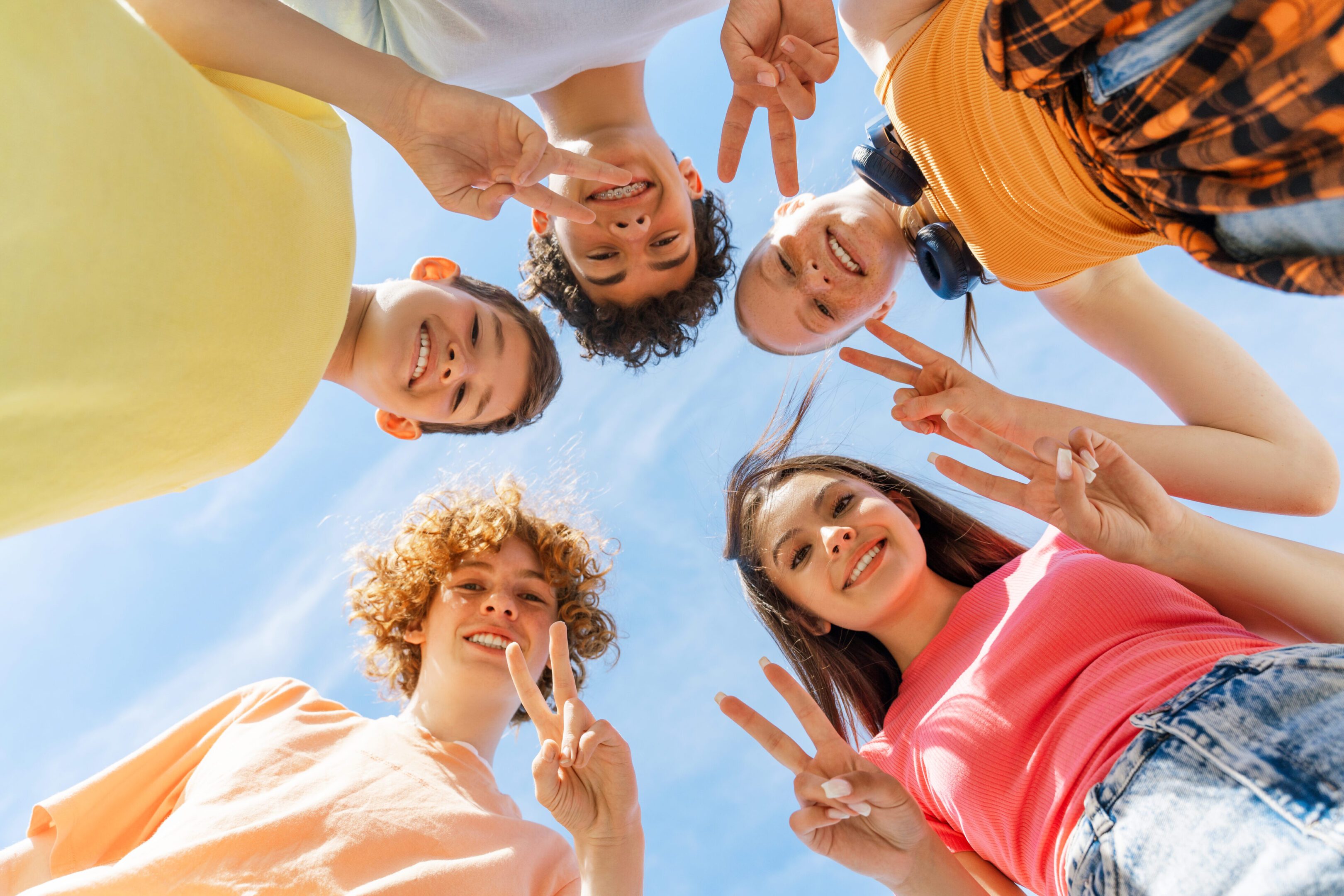 Four friends smiling and posing with peace signs under the blue sky.