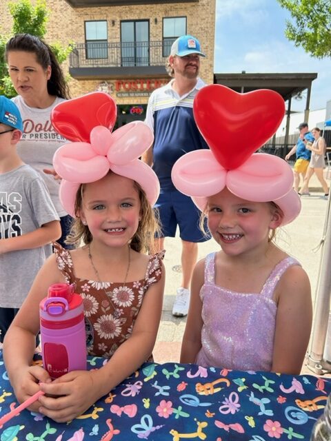 Two girls wearing heart-shaped balloon hats.