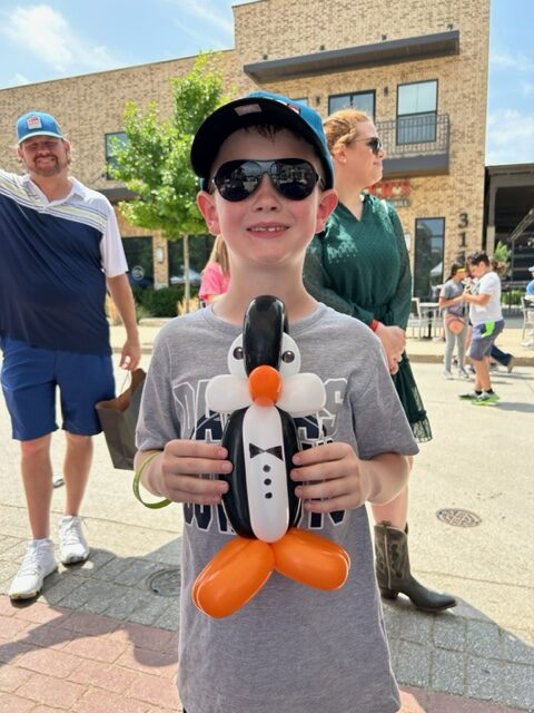 Boy holding penguin balloon at outdoor event.