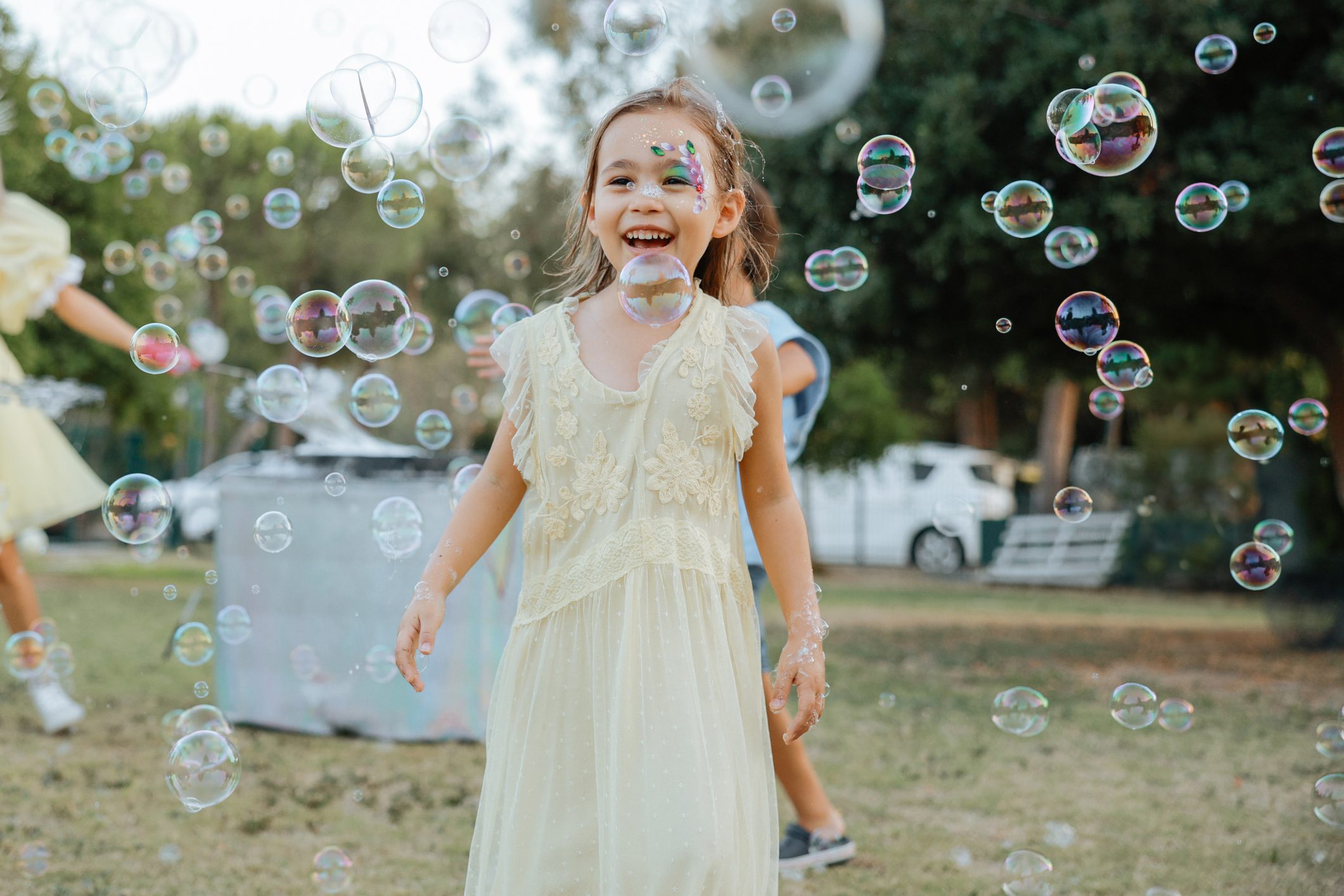 A joyful girl in a white dress playing with bubbles outdoors.