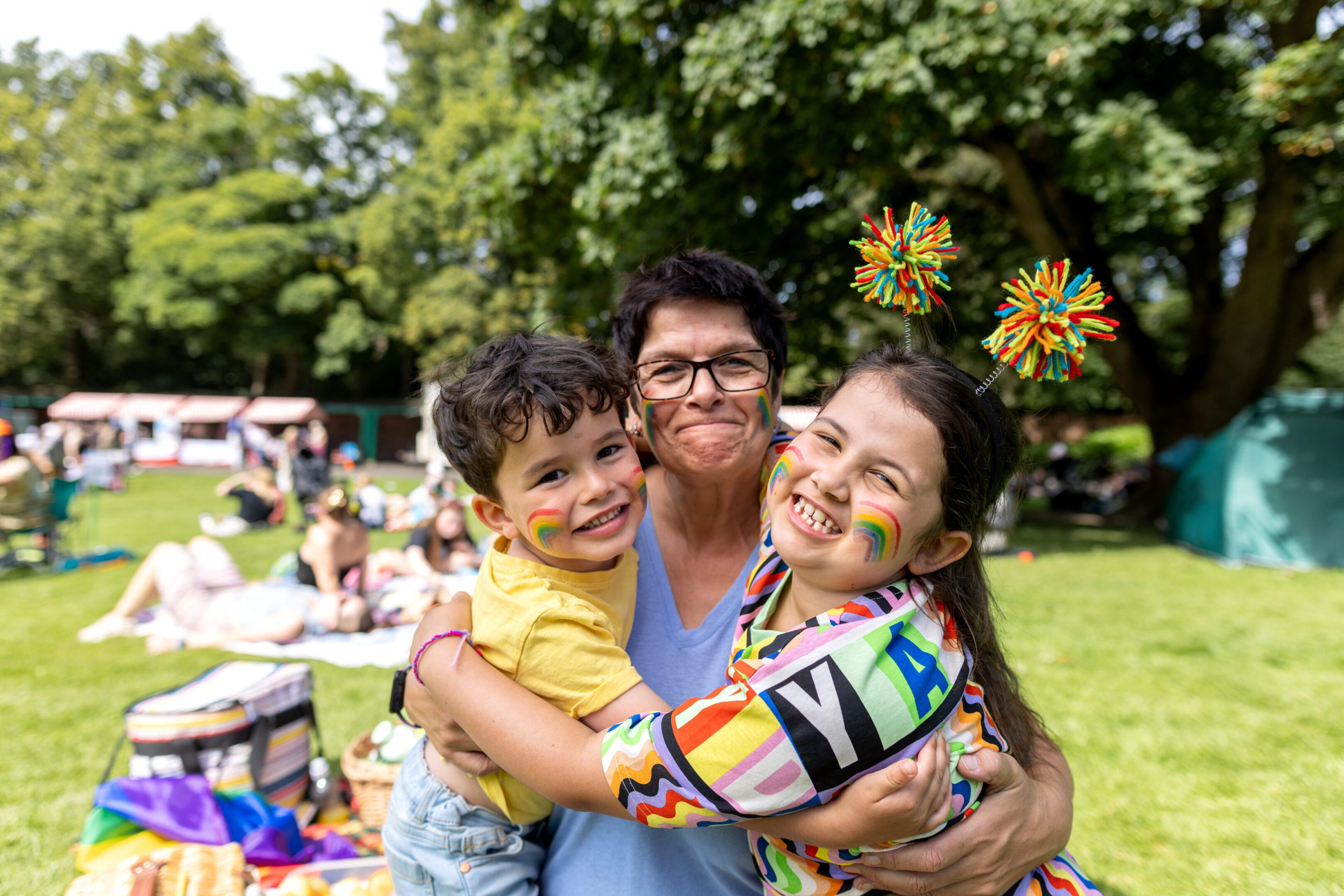 Three people happily hugging outdoors on a sunny day.