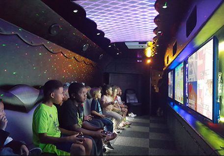 Group of kids playing video games in a dimly lit arcade room.