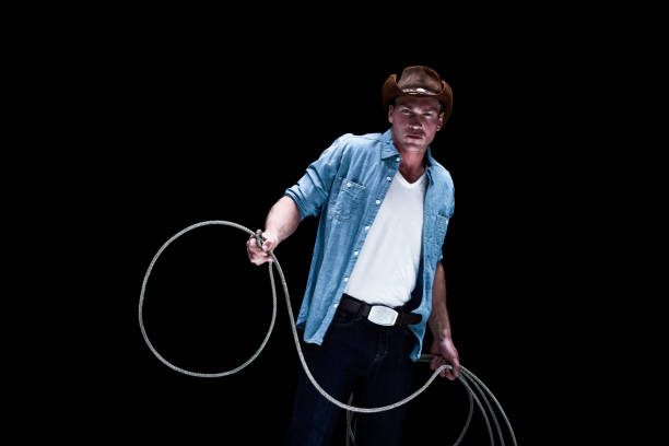 Man in denim shirt holding a coiled rope against a black background.