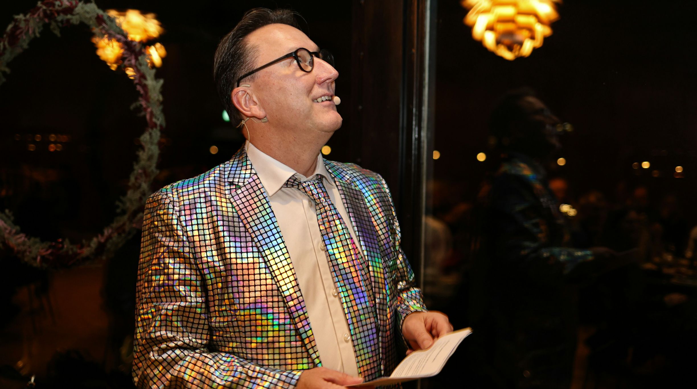 Man in a colorful sequin jacket smiling indoors at night.