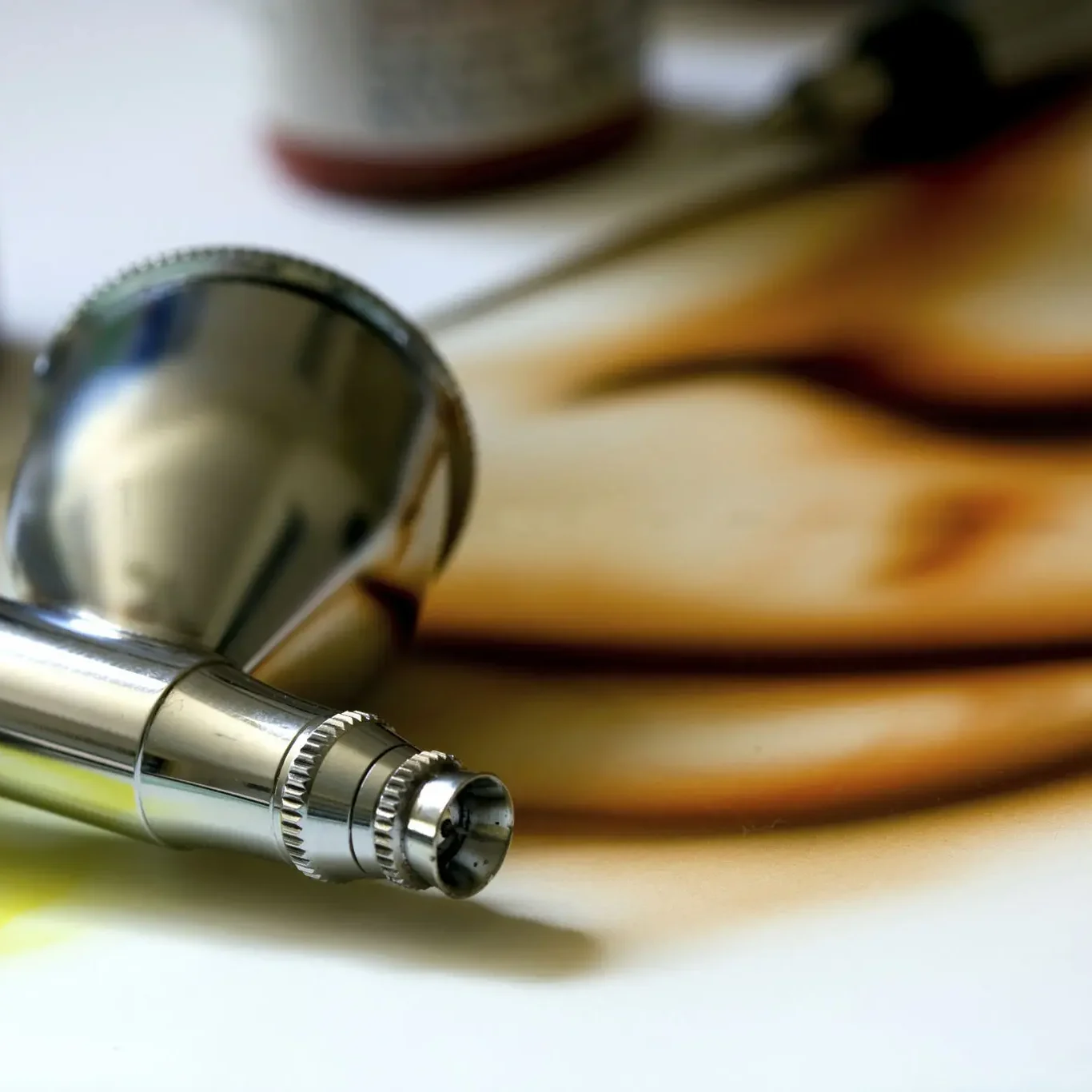 Close-up of a metal airbrush tool on a light surface.