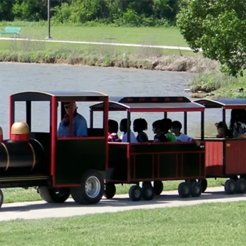 Miniature train with passengers near a lake.